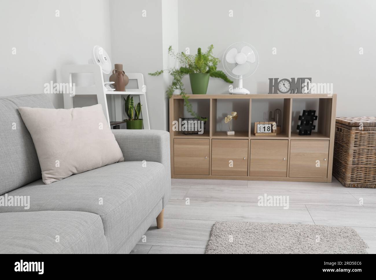 Interior of light living room with clock, houseplant and modern fan on shelving unit Stock Photo