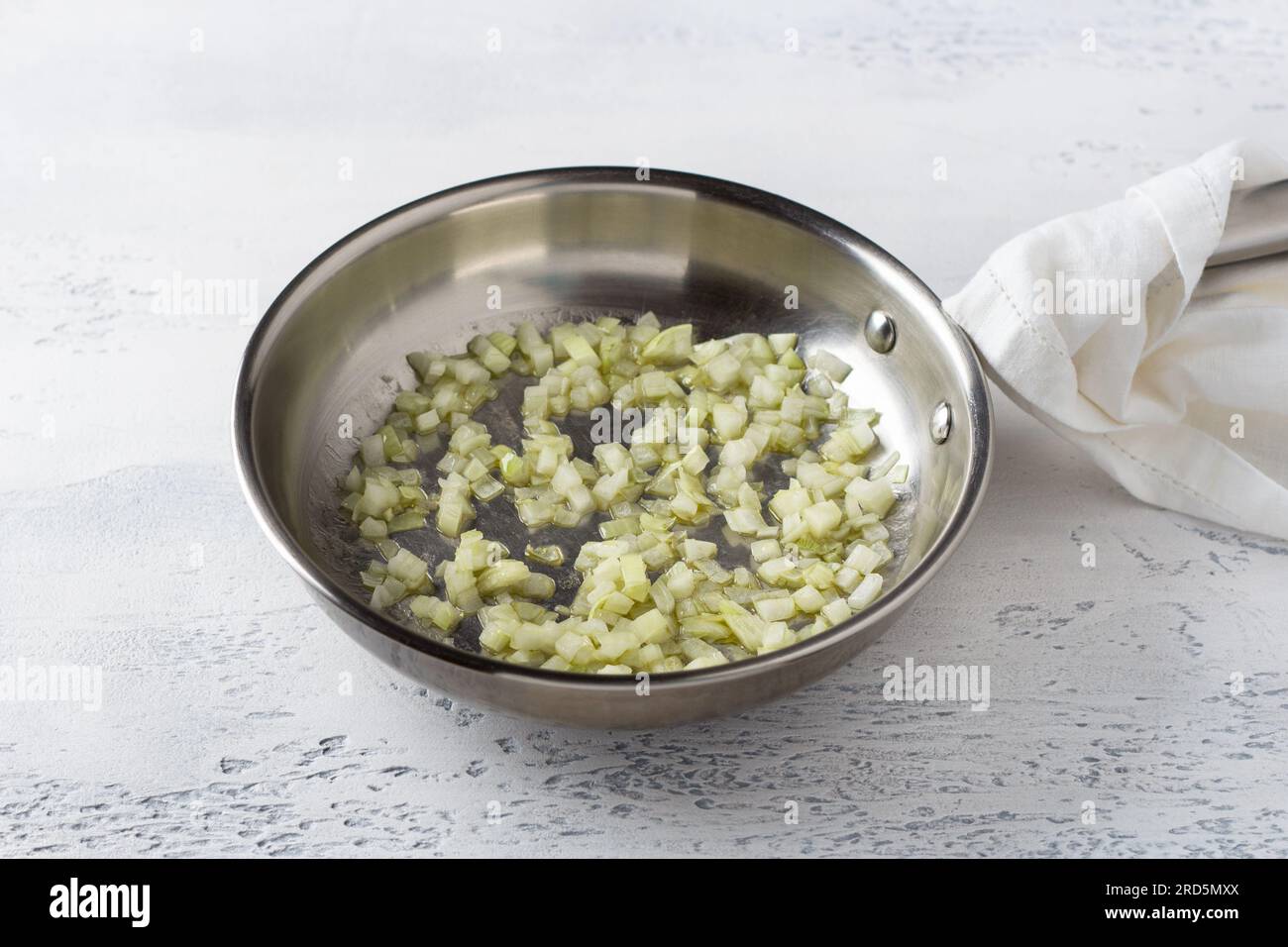 A frying pan with onions fried in butter on a light blue background. Cooking homemade risotto with pear and gorgonzola, step by step, step 2. Stock Photo