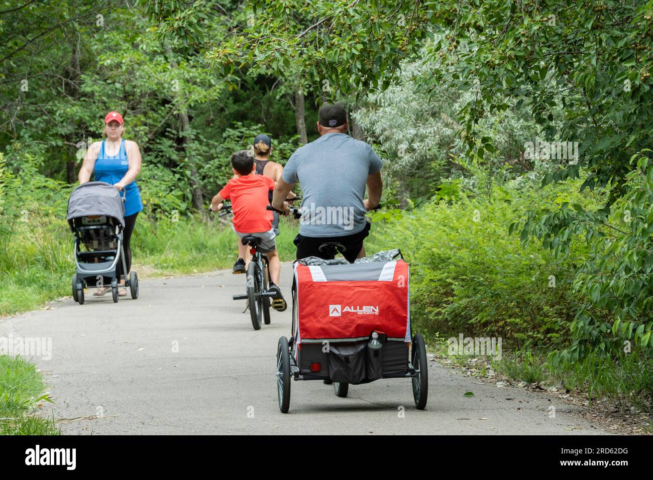 Three Caucasian people riding bikes & one woman walking while pushing a
