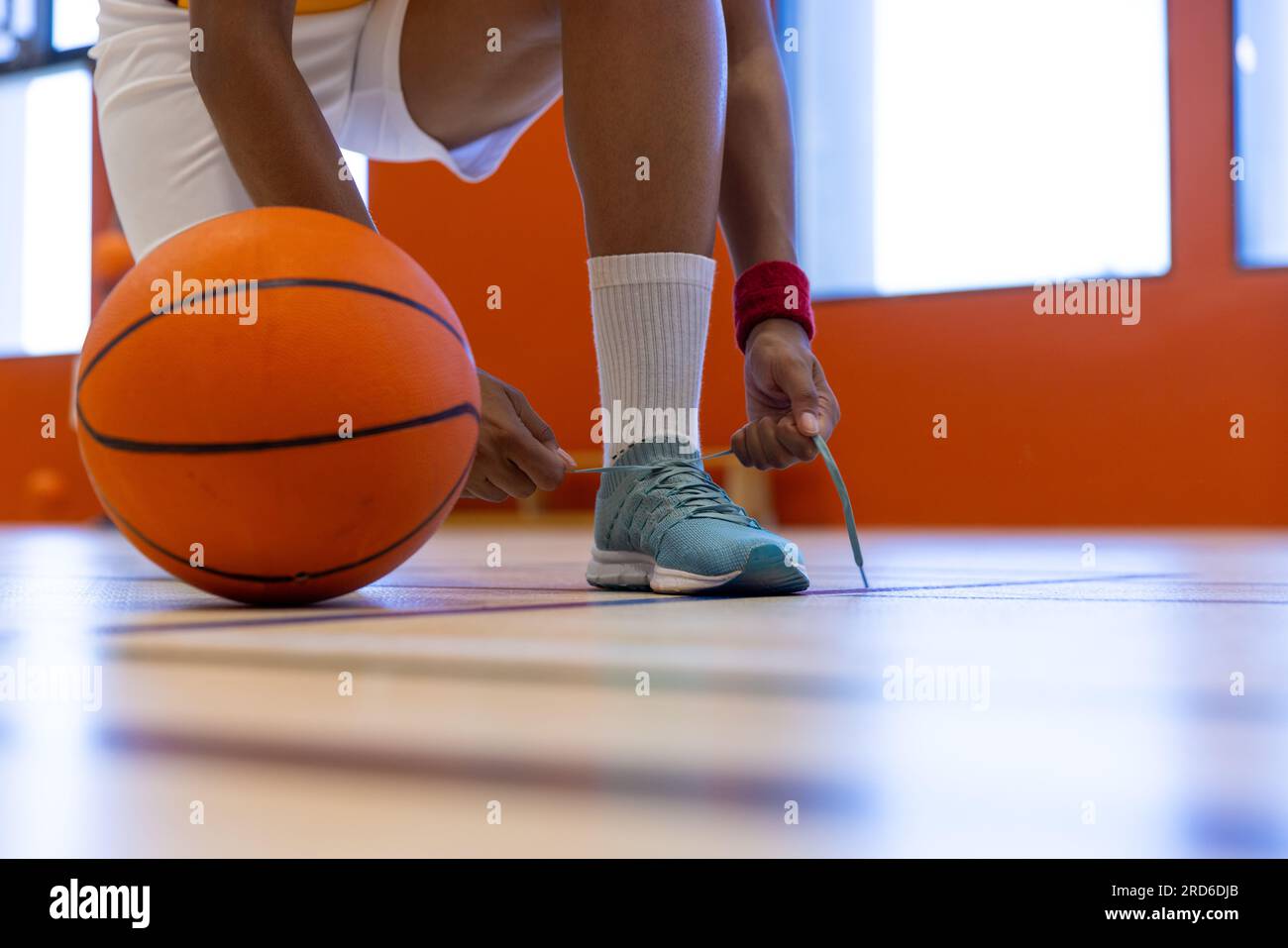 Female basketball player wearing sports clothes and tying shoes at gym