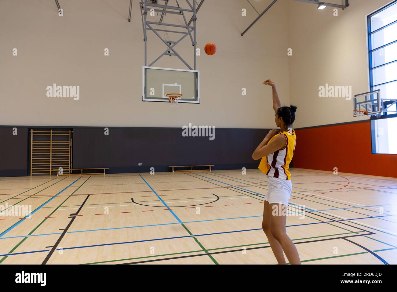 Focused female basketball player wearing sports clothes with number and shooting basketball at