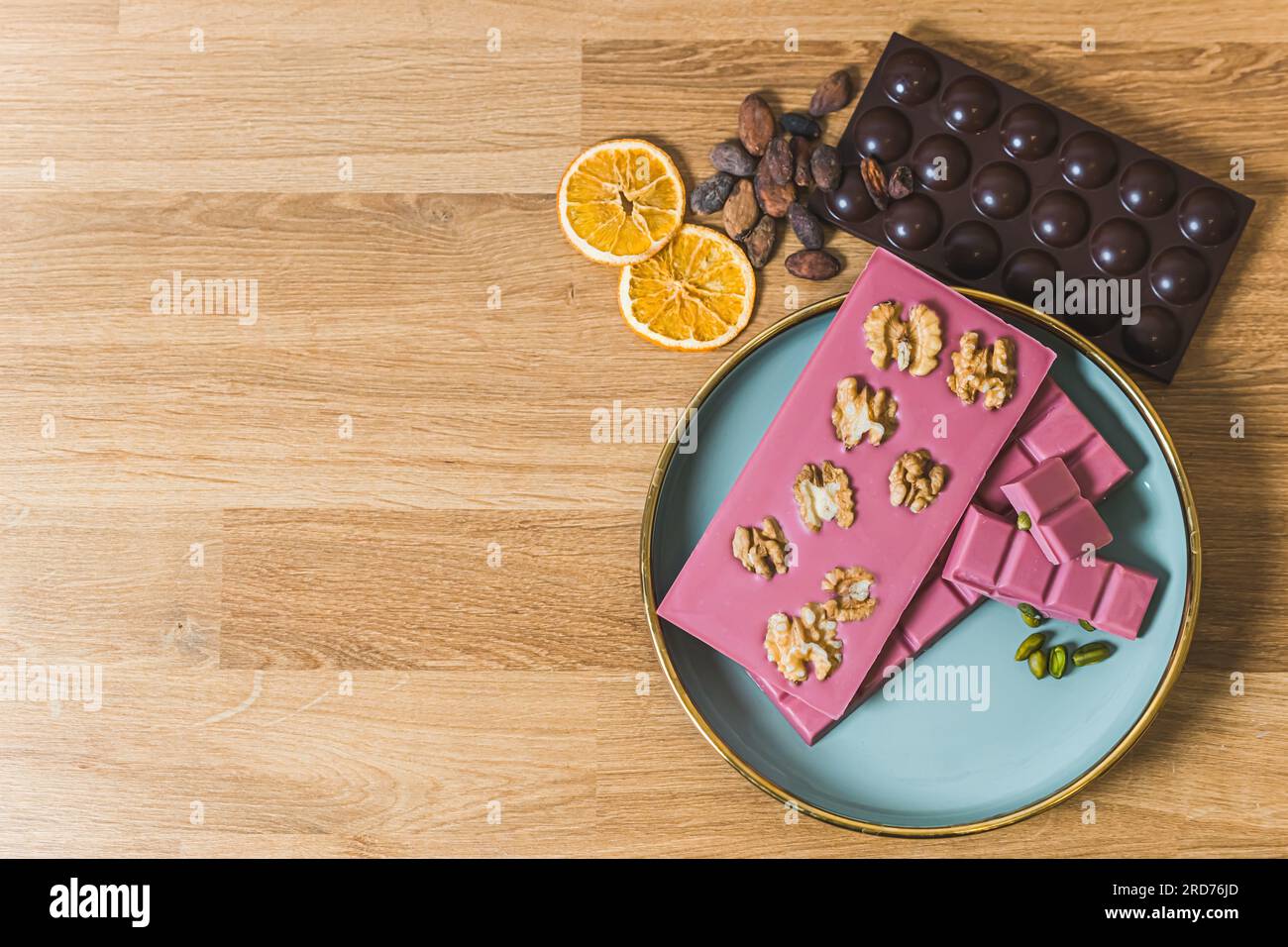 Serving suggestion concept. Brs of ruby aand dark chocolate arrenged on blue plate and wooden table decorated with walnuts slices of orange and cocoa seeds. Copy space. High quality photo Stock Photo