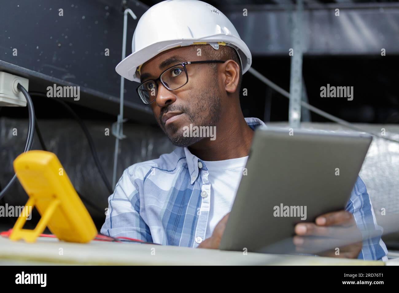 electrician working in roofspace using multimeter and tablet Stock Photo