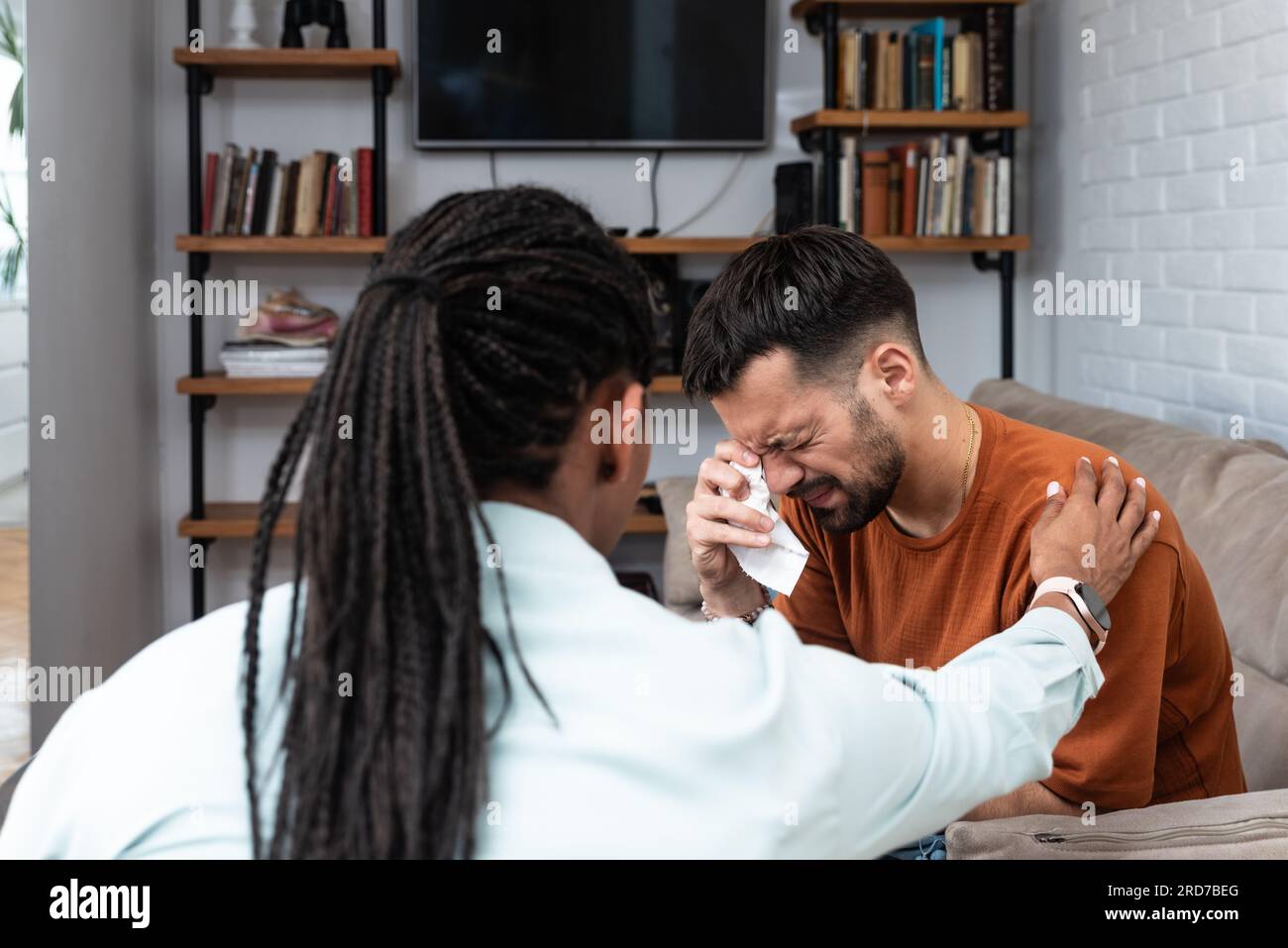 Young depressed man crying talking to mental health counselor during a session in the office. Stressed male at psychotherapy after divorce having emot Stock Photo