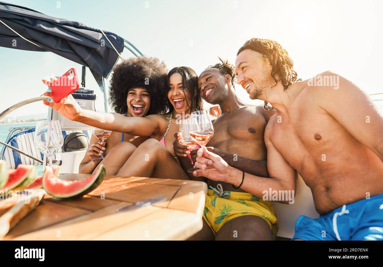 Happy multiracial friends taking selfie while drinking champagne on sail boat - Summer vacation, party and travel concept - Focus on center people fac Stock Photo