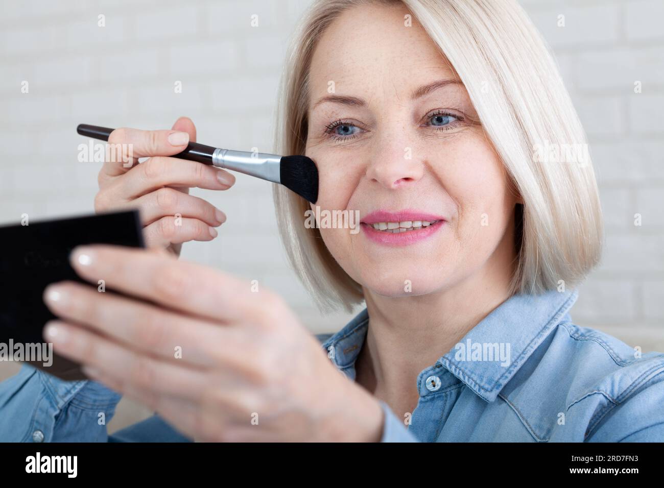 Elegance in Reflection. Captivating shot of a woman skillfully applying makeup before a vanity mirror, creating a timeless beauty ritual. Woman is doi Stock Photo