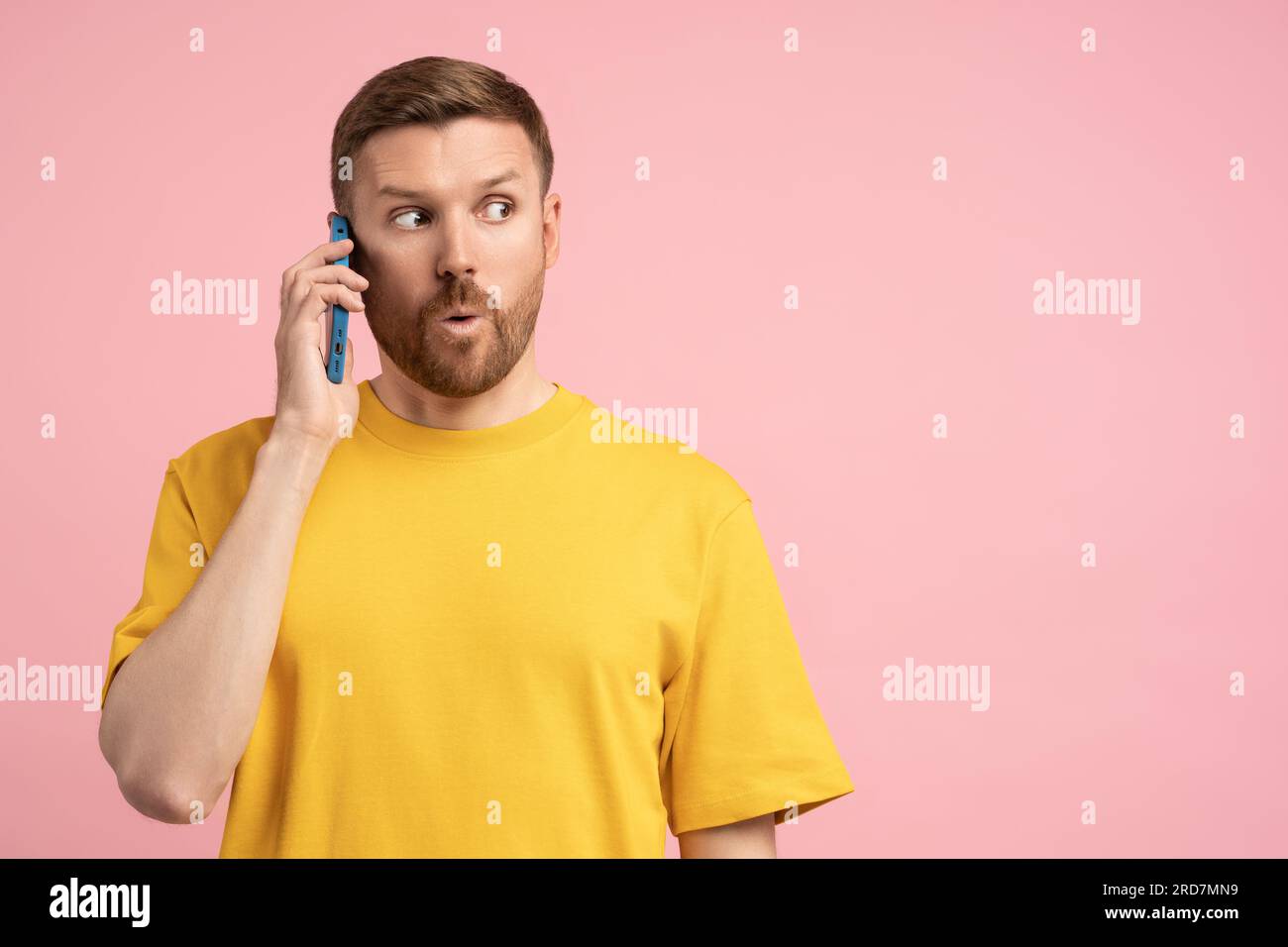 Shocked man holding cellphone surprised pointing wow eyes at copy space over pink studio background Stock Photo