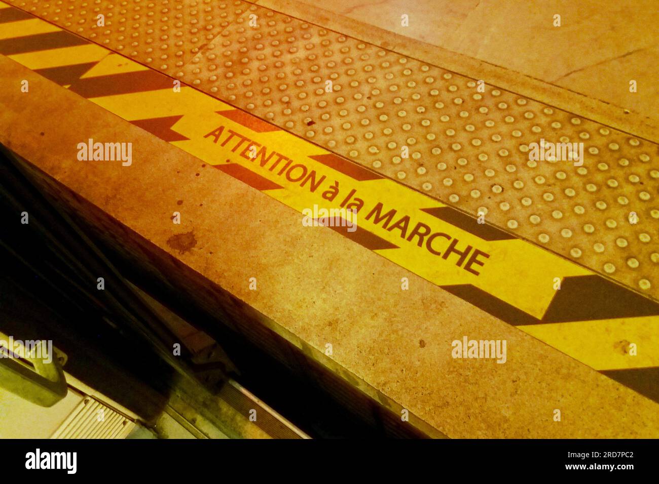 Yellow and black striped warning sign painted on the edge of a subway platform of the Paris Metro saying in french 'Attention à la marche', meaning in Stock Photo