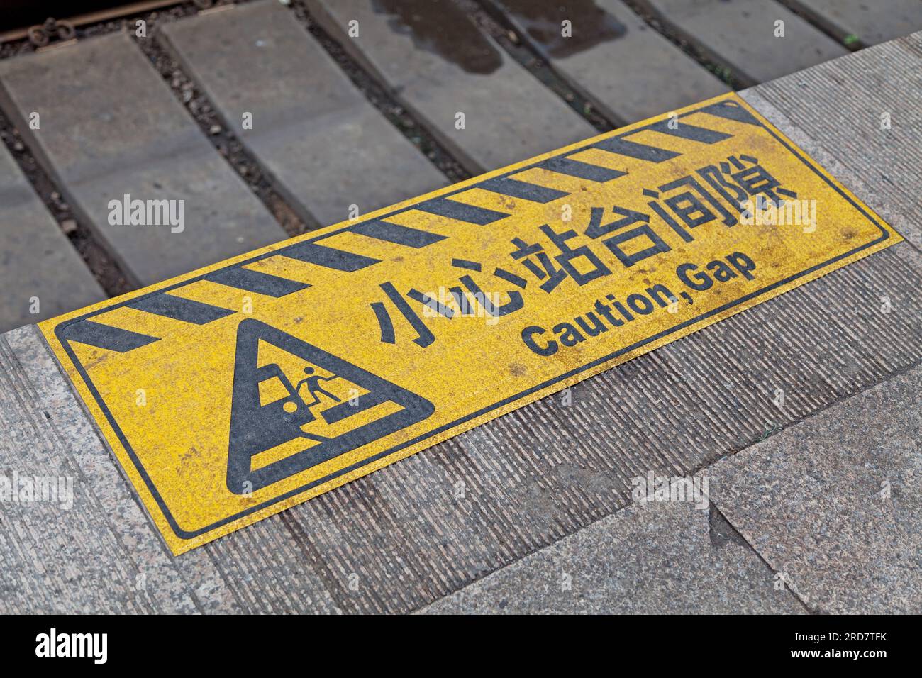 Yellow and black striped warning sign painted on the edge of a train platform of the Beijing Railway Station saying in Chinese 'Mind the gap'. Stock Photo