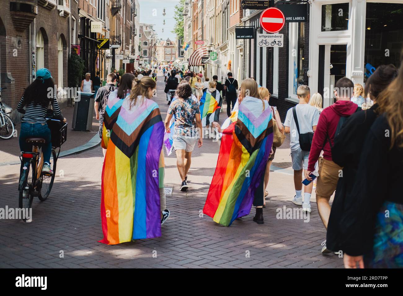 Amsterdam, North Holland, Netherlands – August 6, 2022: A crowd of people including two young girls in New Progress Pride flags walk through streets Stock Photo