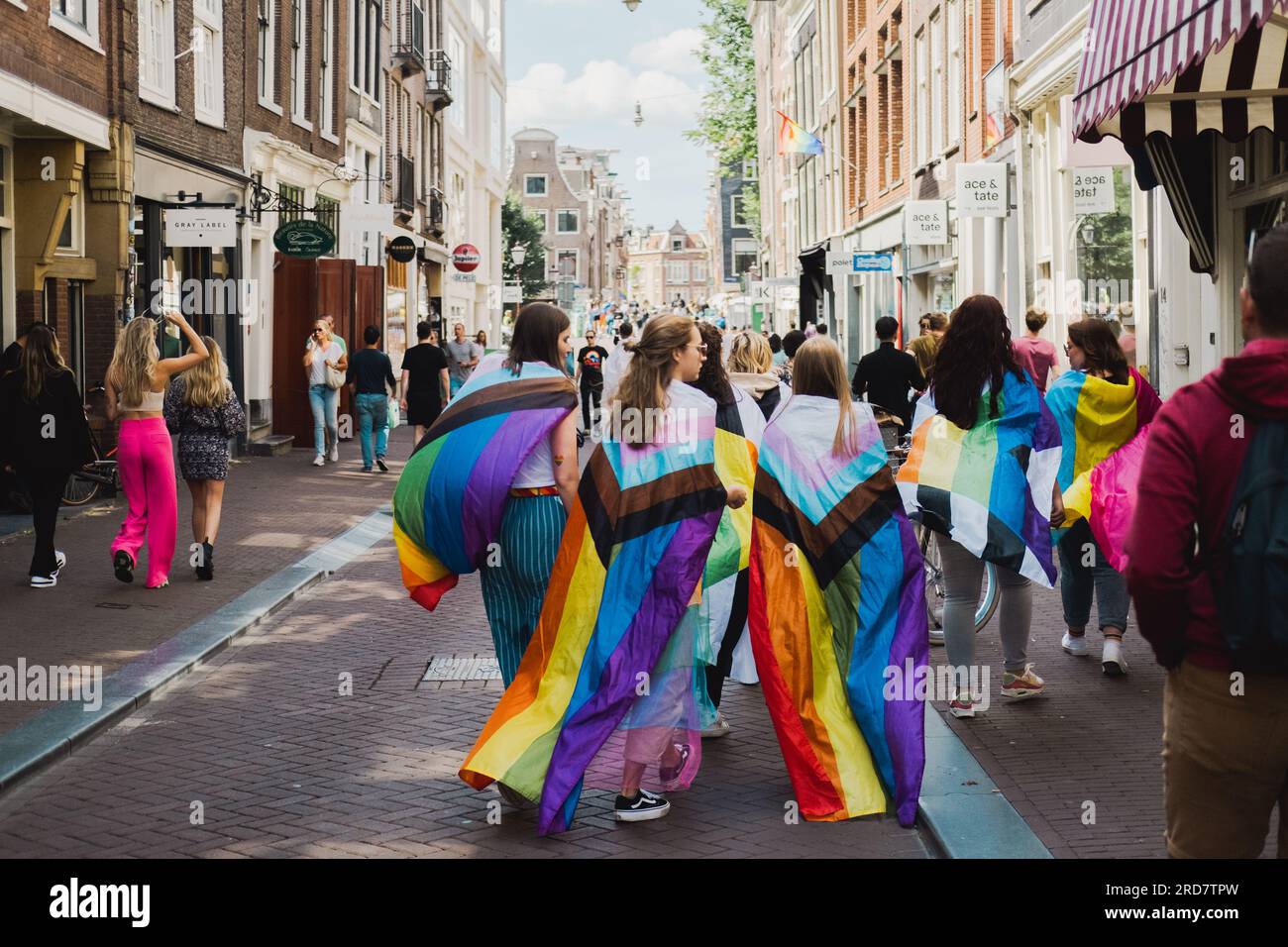 Amsterdam, North Holland, Netherlands – August 6, 2022: A group of young girls draped over with New Progress Pride flags walk through streets Stock Photo