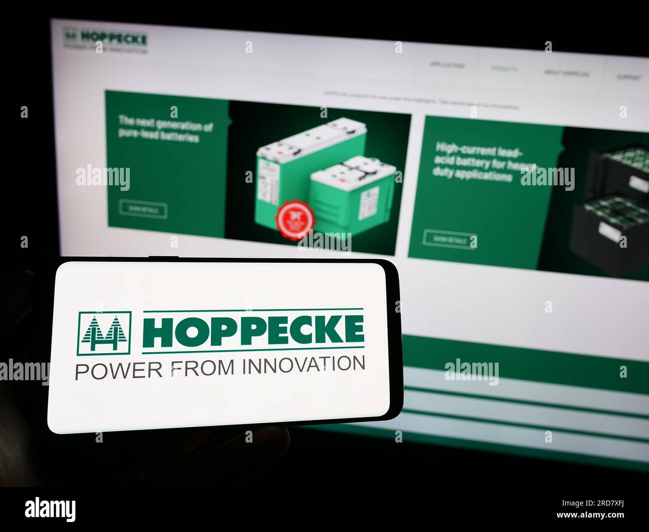 Person holding mobile phone with logo of German company Accumulatorenwerke Hoppecke on screen in front of web page. Focus on phone display. Stock Photo