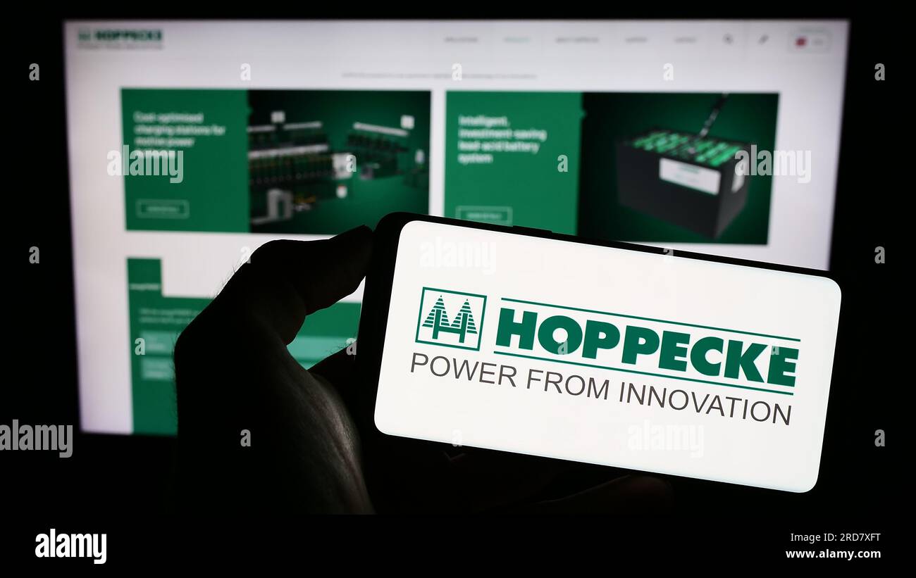 Person holding cellphone with logo of German company Accumulatorenwerke Hoppecke on screen in front of business webpage. Focus on phone display. Stock Photo