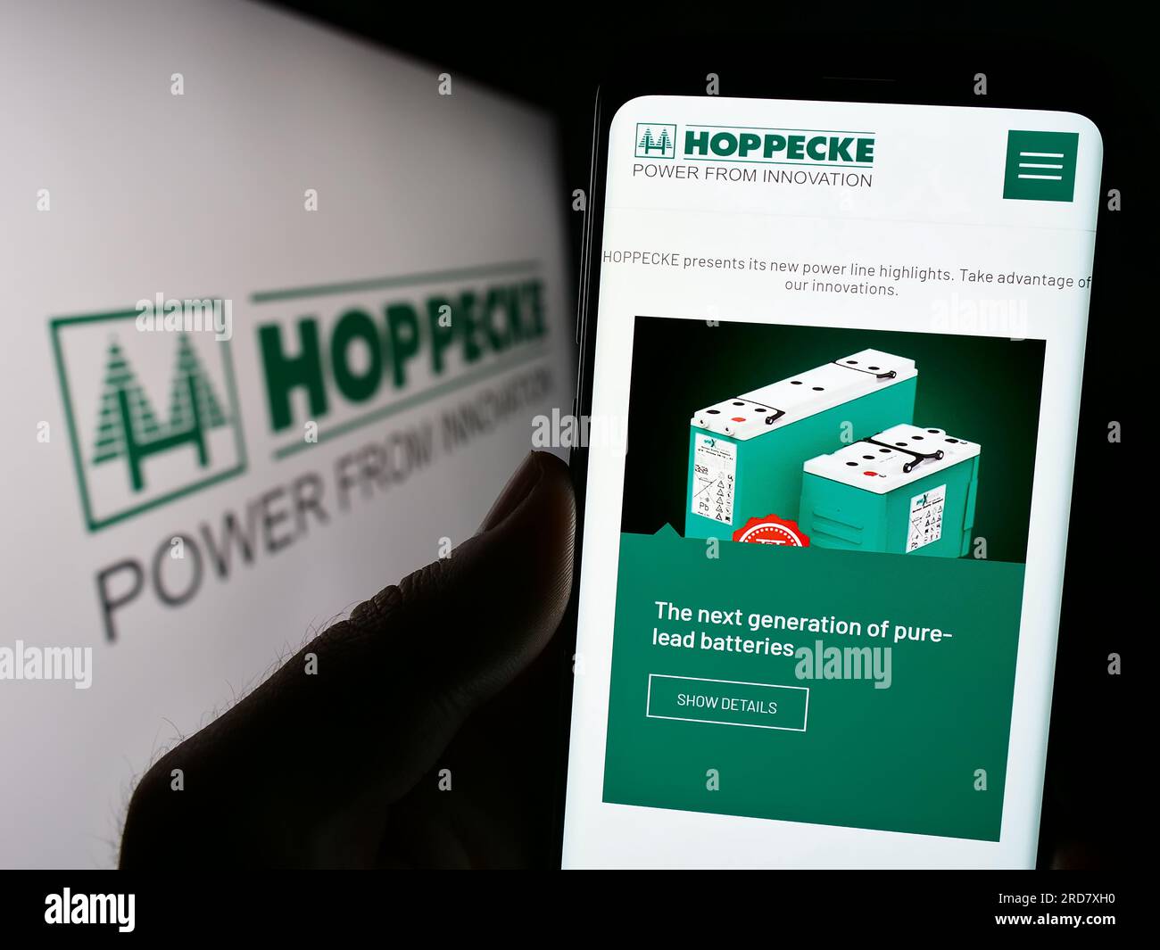 Person holding smartphone with webpage of German company Accumulatorenwerke Hoppecke on screen in front of logo. Focus on center of phone display. Stock Photo