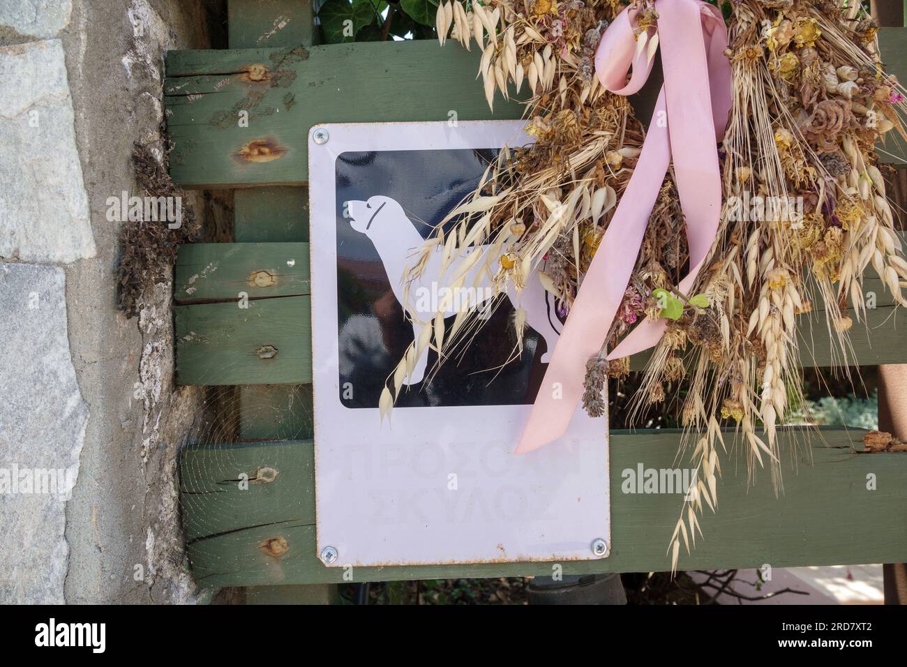 A beware of the dog sign on a wooden fence with corn dolly and pink ribbon, Kefalonia, Greece Stock Photo