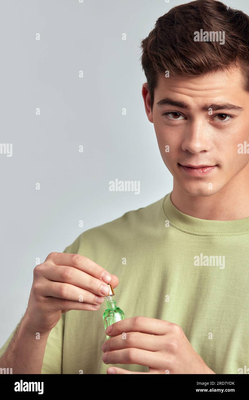 Young handsome brown haired guy holding a vial of beauty serum in his hand preparing to apply it on his face. Caucasian man uses beauty products in hi Stock Photo