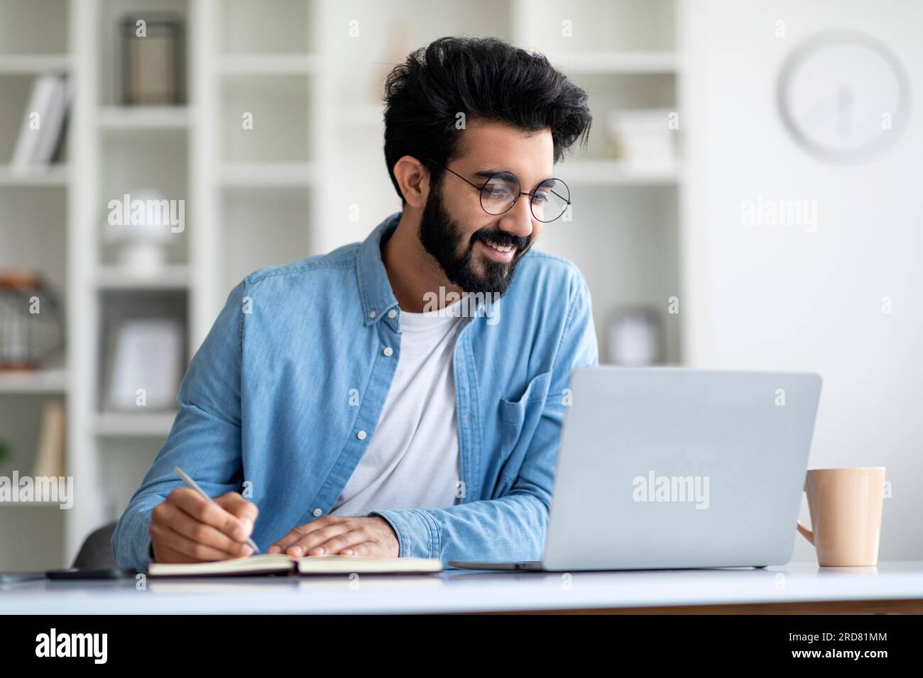 Online Lesson. Smiling Young Indian Man Using Laptop And Taking Notes Stock Photo