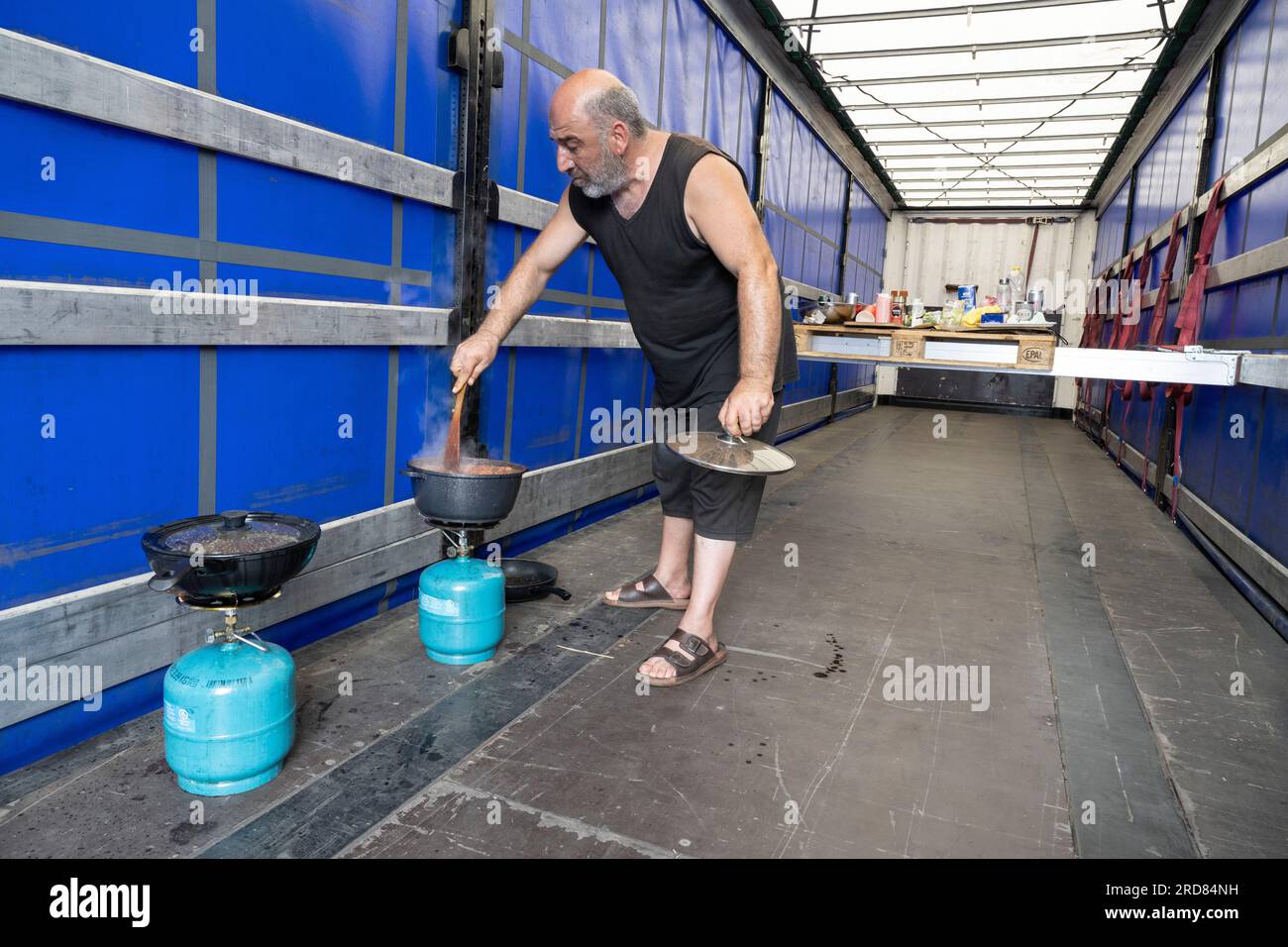 19 July 2023, Hesse, Gräfenhausen: Truck driver Zurab from Georgia prepares dinner on the loading area of his truck. Together with other drivers from a Polish freight forwarding company, he has gone on strike at the Gräfenhausen rest area on the A5 in Hesse to demand outstanding wages. Photo: Boris Roessler/dpa Stock Photo