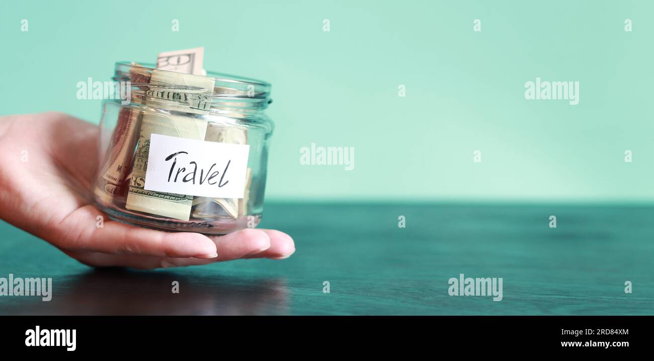 Close-up of a young woman's hand holding a glass jar of money. Piggy bank with dollars for travel. The hand holds a jar of money, travel, savings. Fin Stock Photo