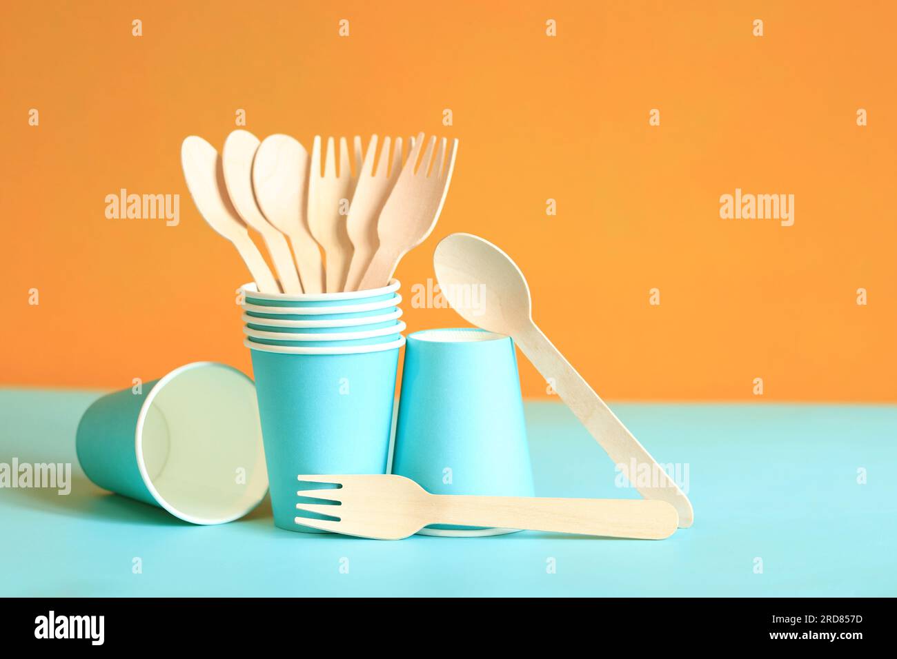 Wooden disposable forks and spoons in a blue paper cup. Selective focus. Eco friendly disposable kitchen utensils on orange background, copy space. Ec Stock Photo