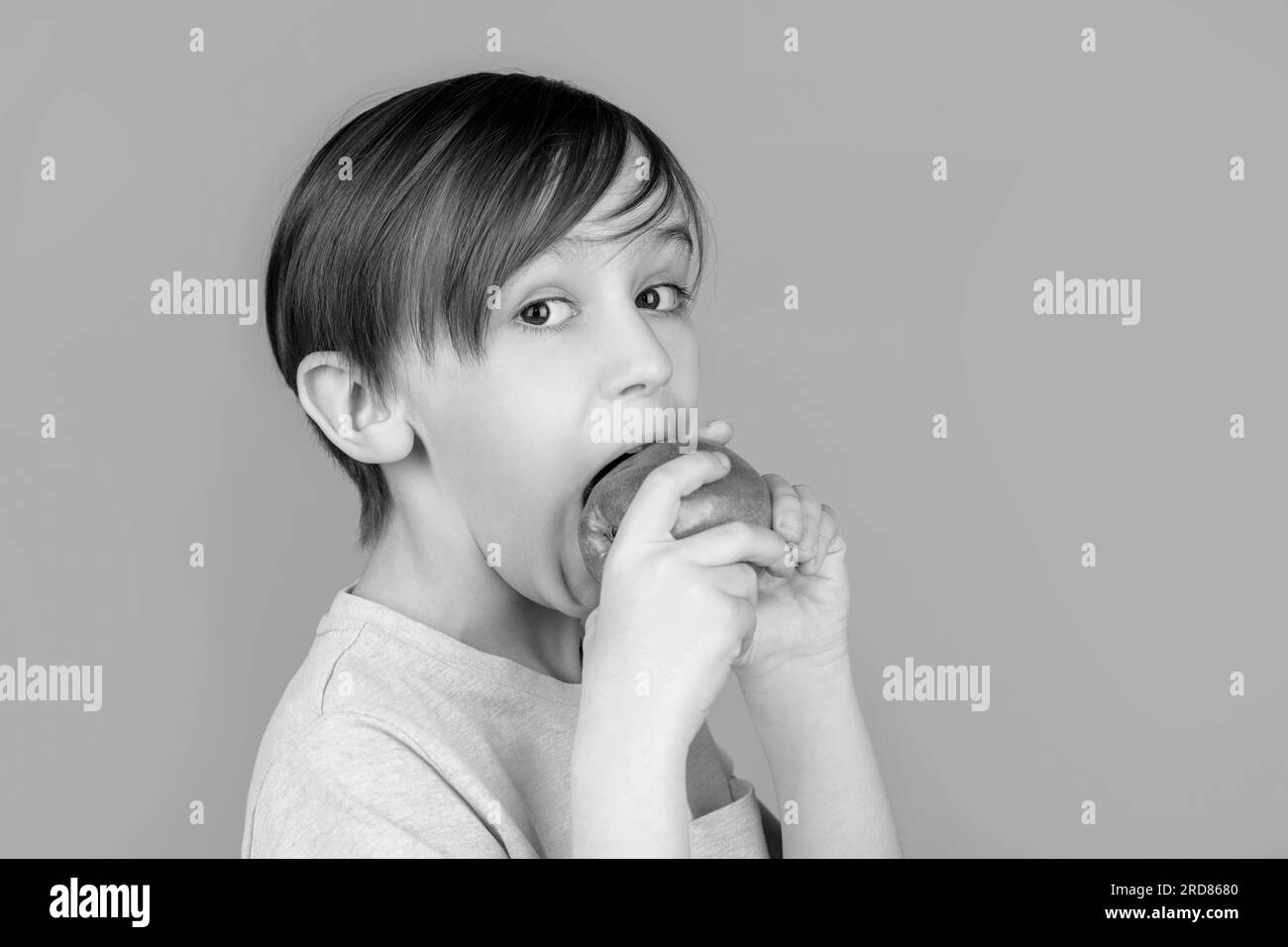 Boy eating apple and smiling. Boy smiles and has healthy white teeth. Little boy eating apple. Boy apples showing. Child with apples. Black and white Stock Photo