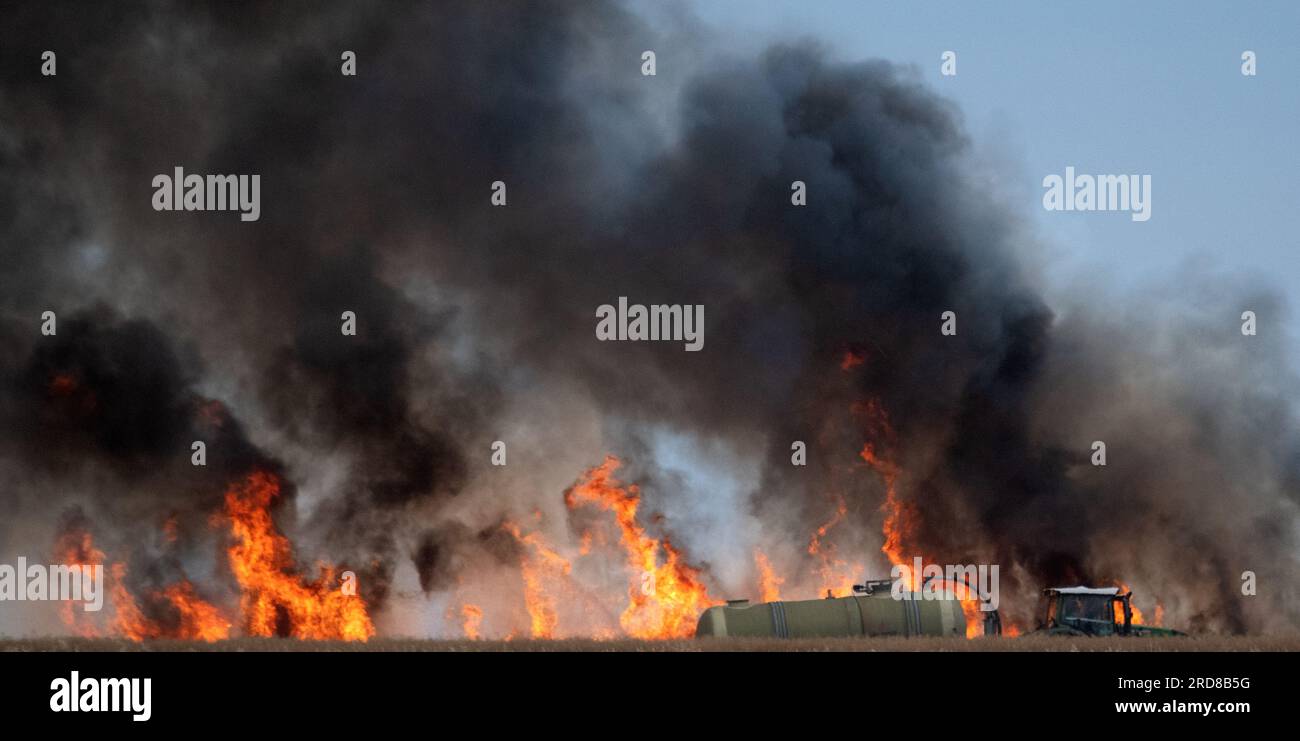 Leipzig, Germany. 19th July, 2023. Dark clouds of smoke rise from a field fire near Leipzig. A slurry tanker extinguishes with water. Credit: Ralf Hirschberger/dpa/Alamy Live News Stock Photo