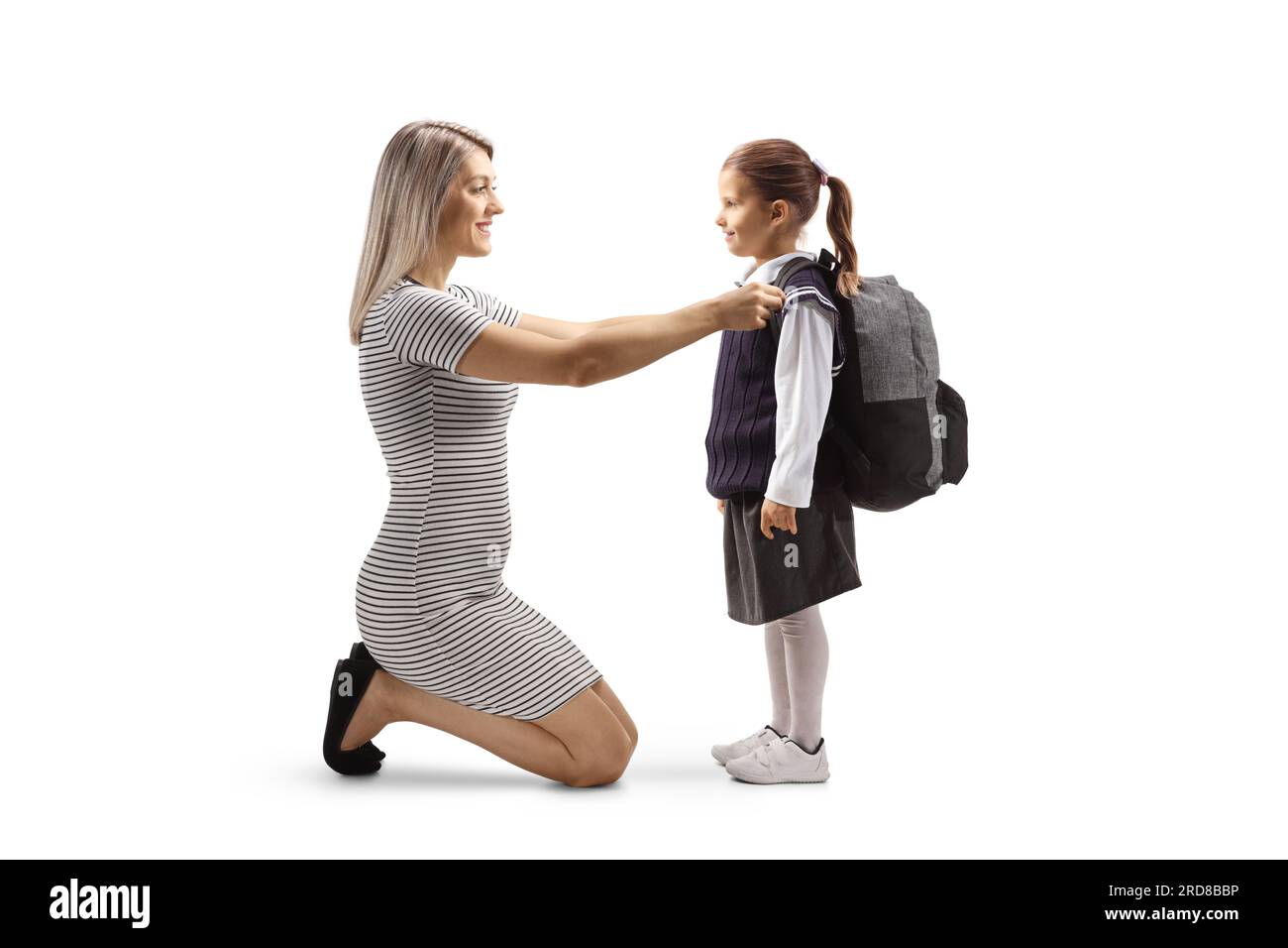 Full length profile shot of a mother helping a daughter to get ready for school with a backpack isolated on white background Stock Photo