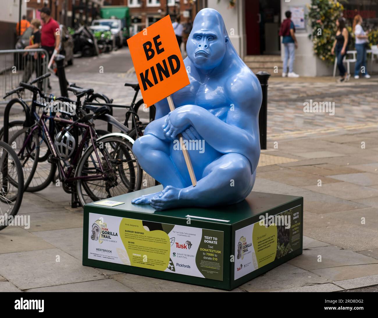 Blue gorilla sculpture holding 'Be Kind' placard in Covent Garden. Artwork by Barnaby Barford, part of the Tusk Gorilla Trail in central London. Stock Photo