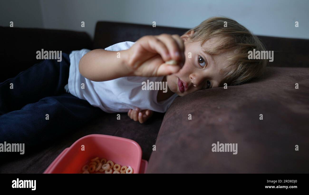 Child eating cereal little boy snacking lying on couch Stock Photo Alamy