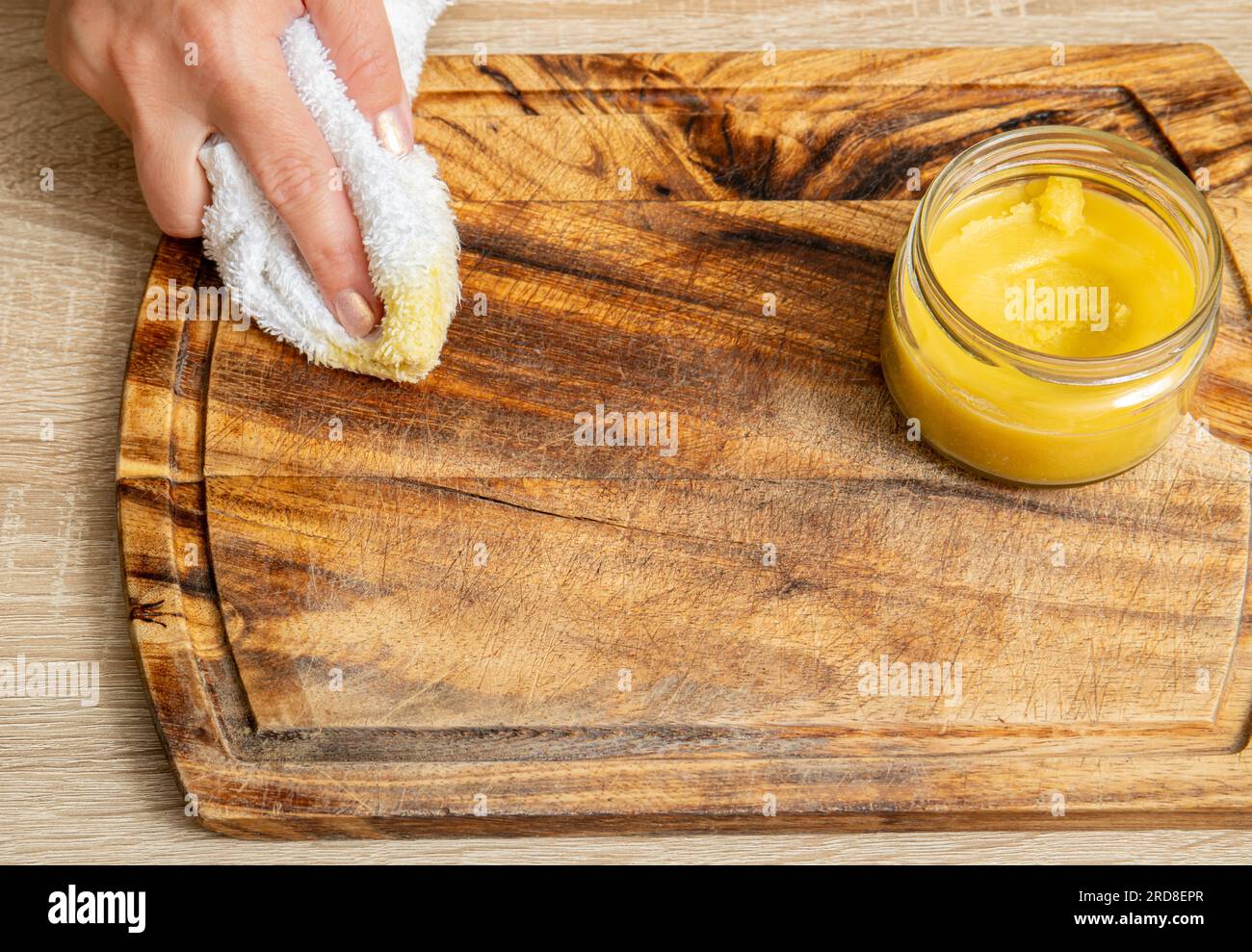 Woman hands apply homemade beeswax wood treatment polish to restore natural wood cutting board. Beeswax, olive oil and essential oil, soft cloth. Stock Photo