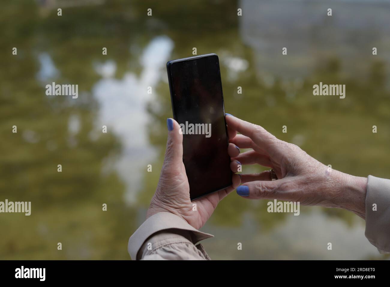 elderly woman's hands holding cell phone in a lake Stock Photo