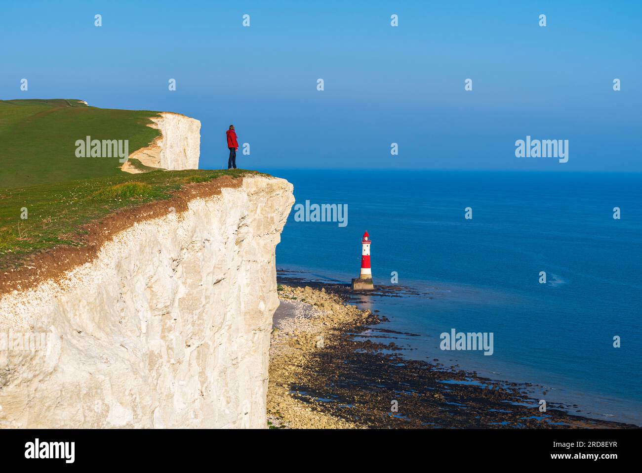 Tourist stands on top of the cliff overlooking Beachy Head lighthouse