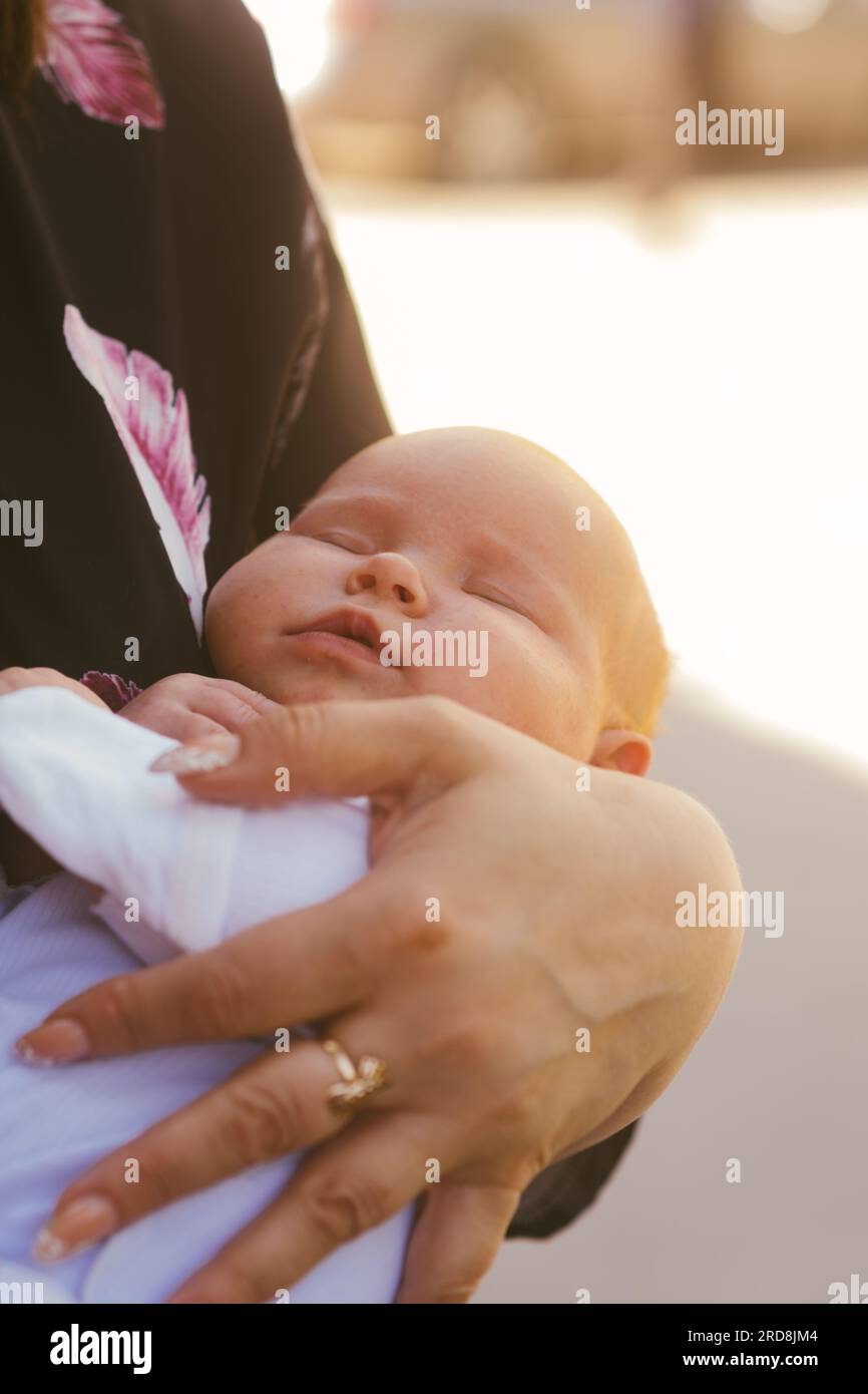 Mom cradles a newborn baby standing on the street. The child sleeps in