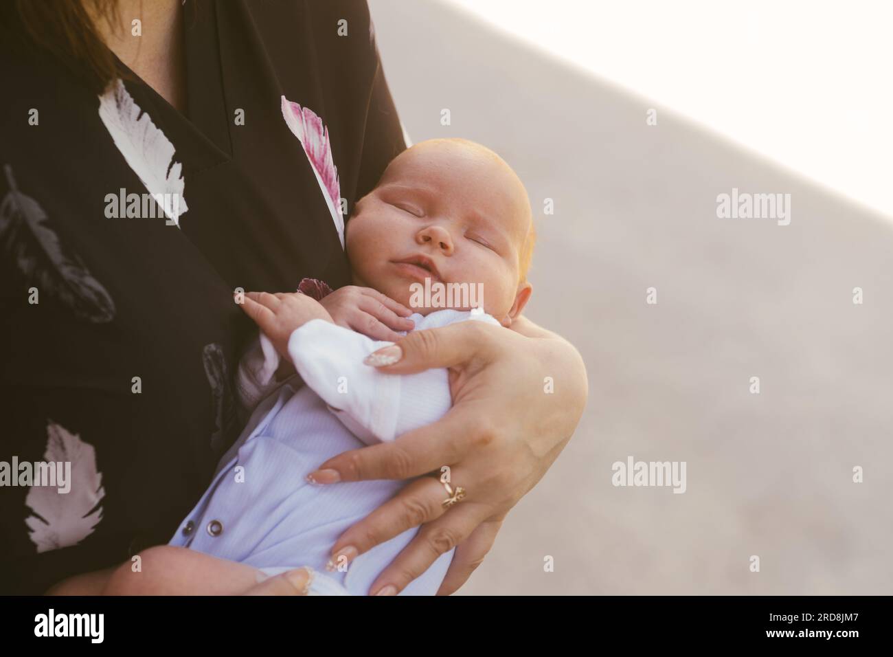 Mom cradles a newborn baby standing on the street. The child sleeps in