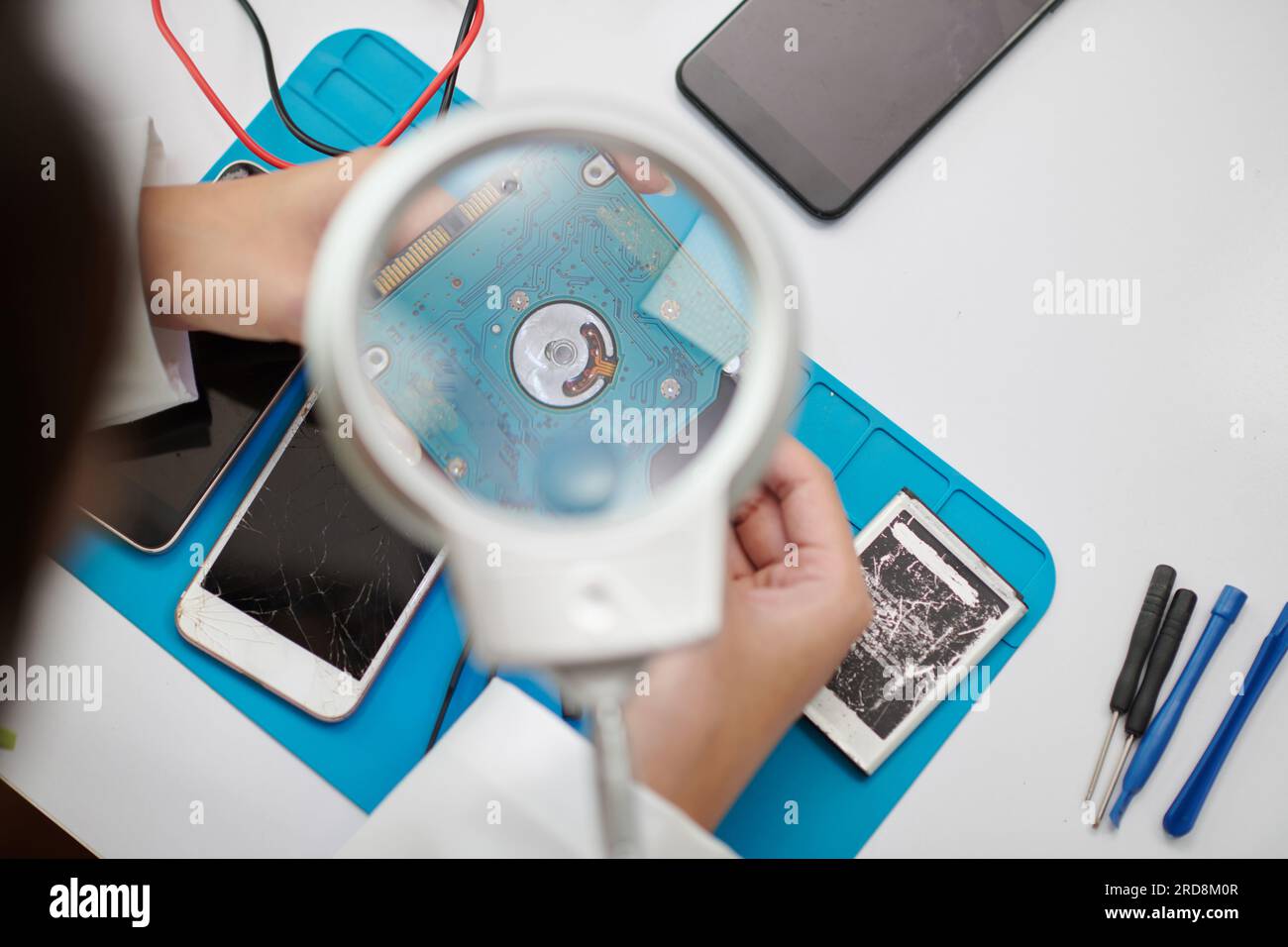 Technician looking through magnifying glass when examining computer hard drive Stock Photo