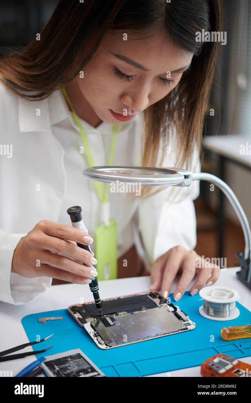 Young woman using magnifying glass when disassembling smartphone Stock Photo