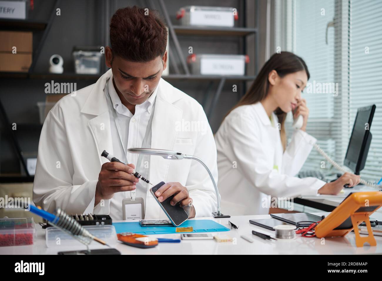 Technician reassembling smartphone when manager talking on phone with client Stock Photo