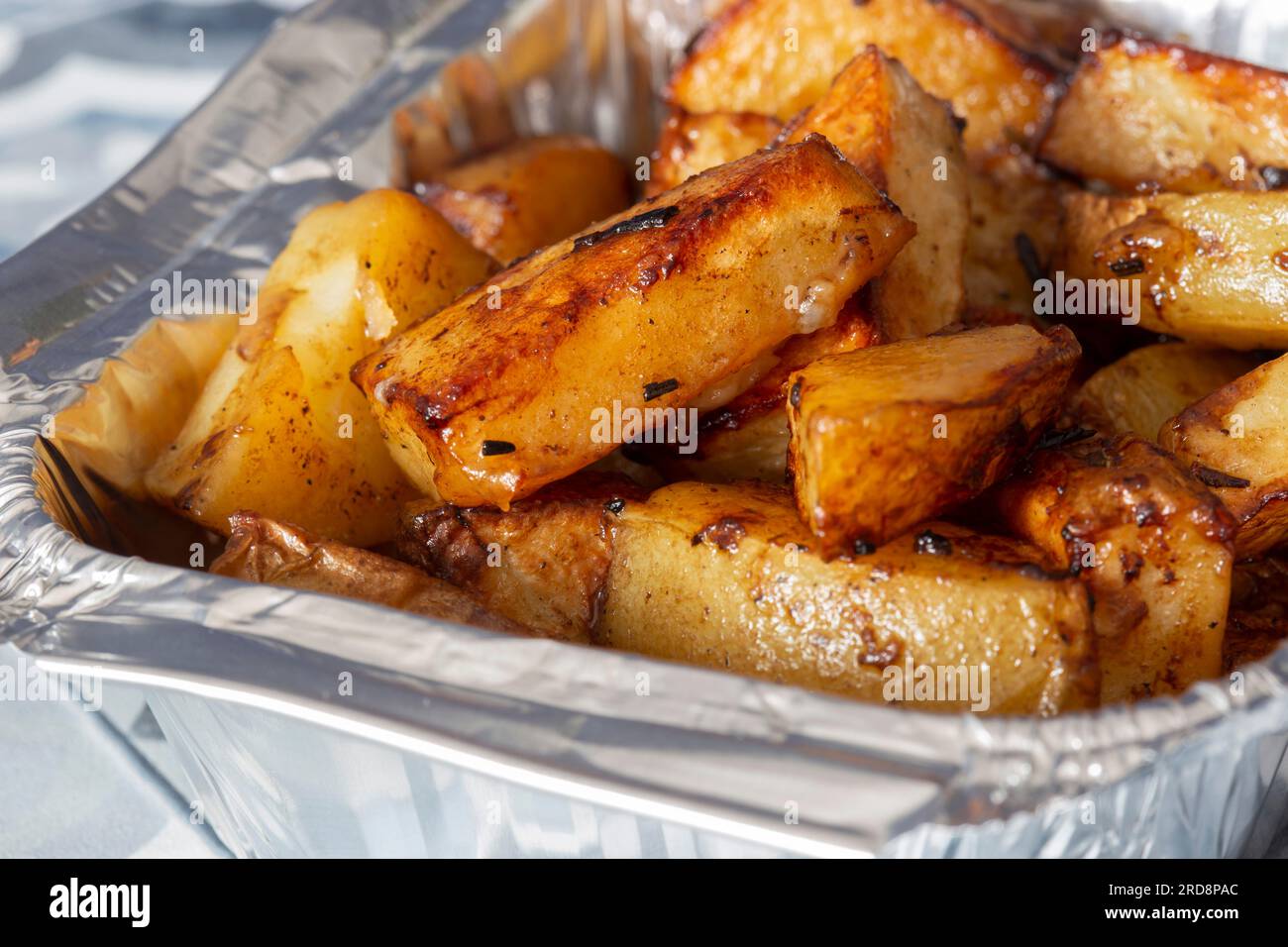 Mini roast potatoes in a takeaway foil tray carton. On a blue tile