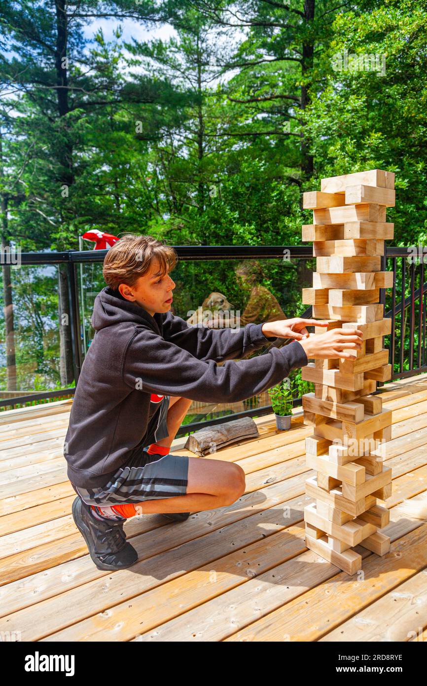 Teenaged boy playing with a large Jenga tower at a lakeside cottage in Muskoka Ontario Canada Stock Photo