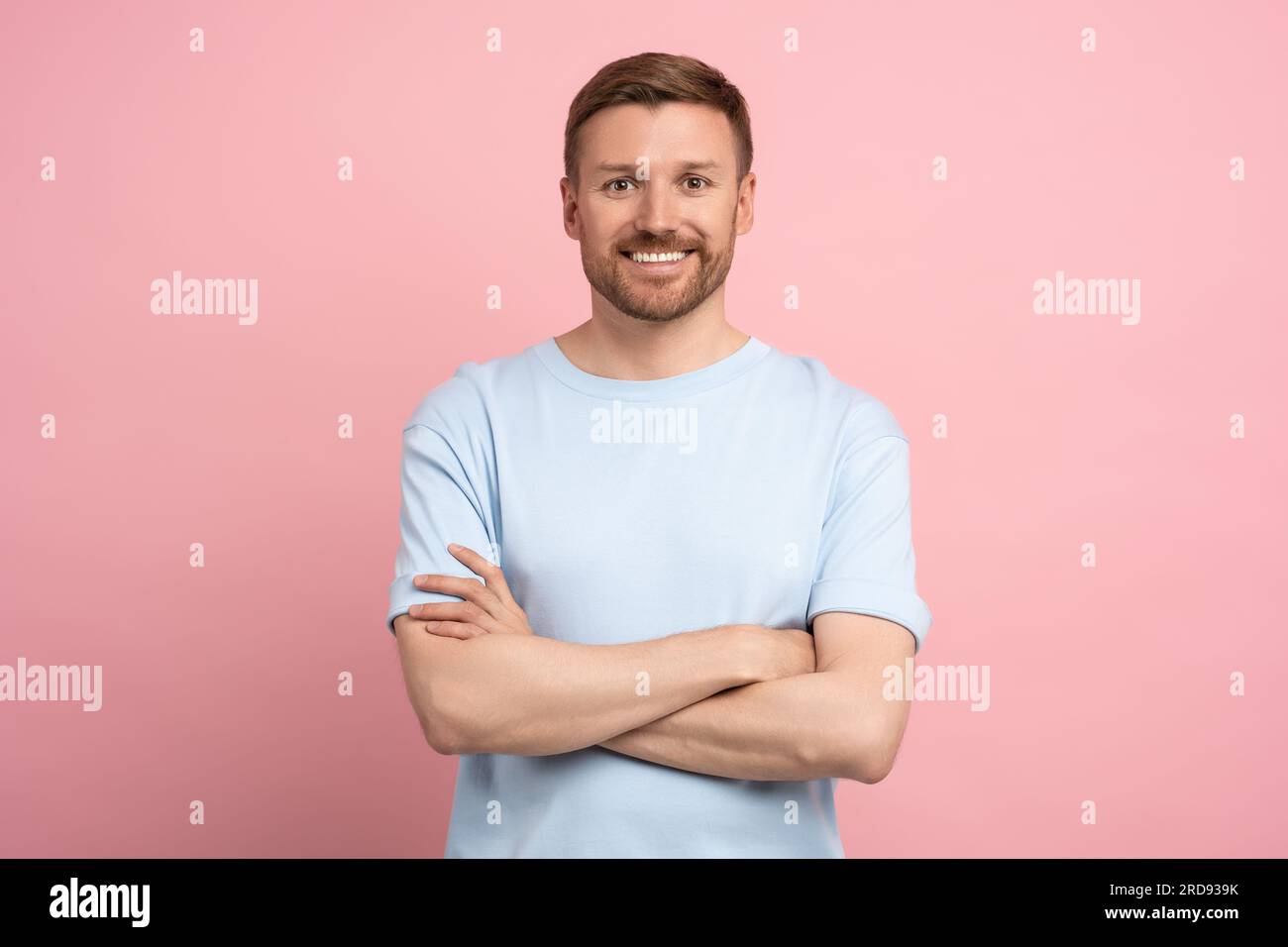 Happy man white teeth smiling with crossed arms look at camera standing isolated on pink studio wall Stock Photo