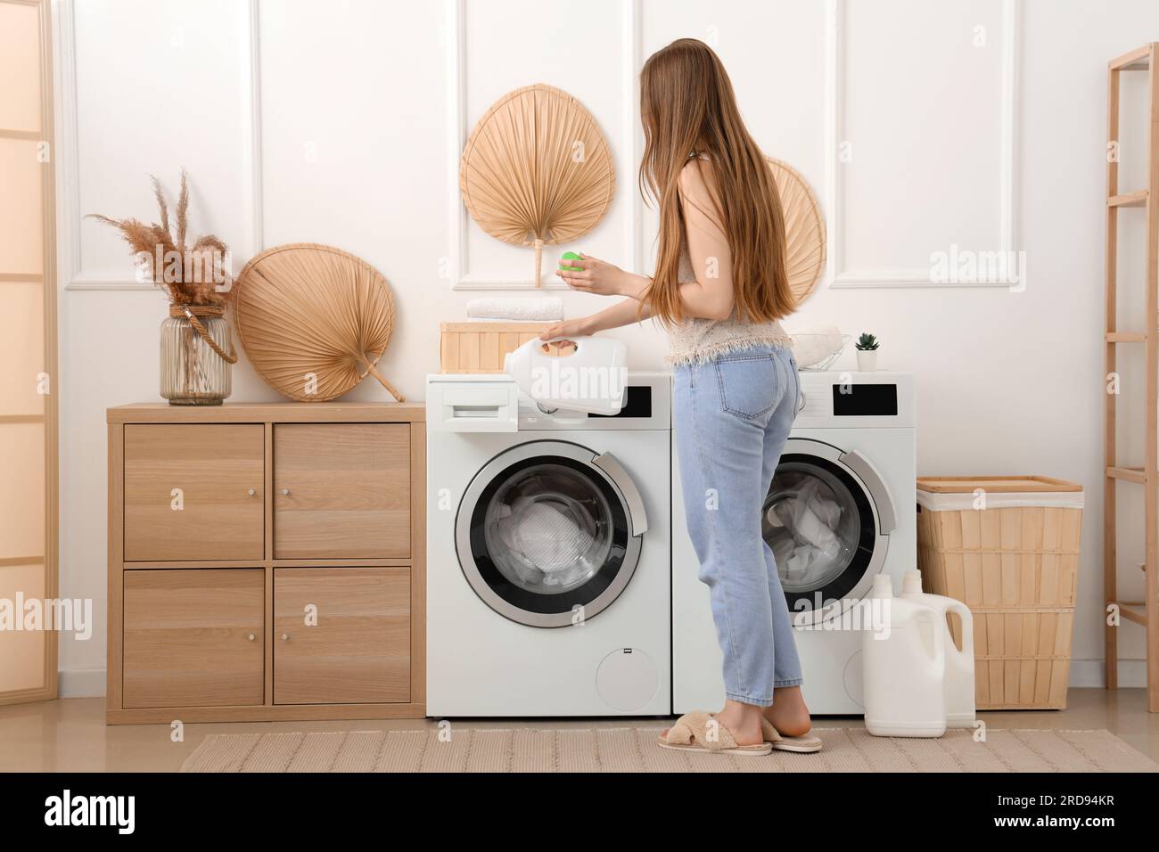 Woman adding detergent into washing machine in laundry room Stock Photo