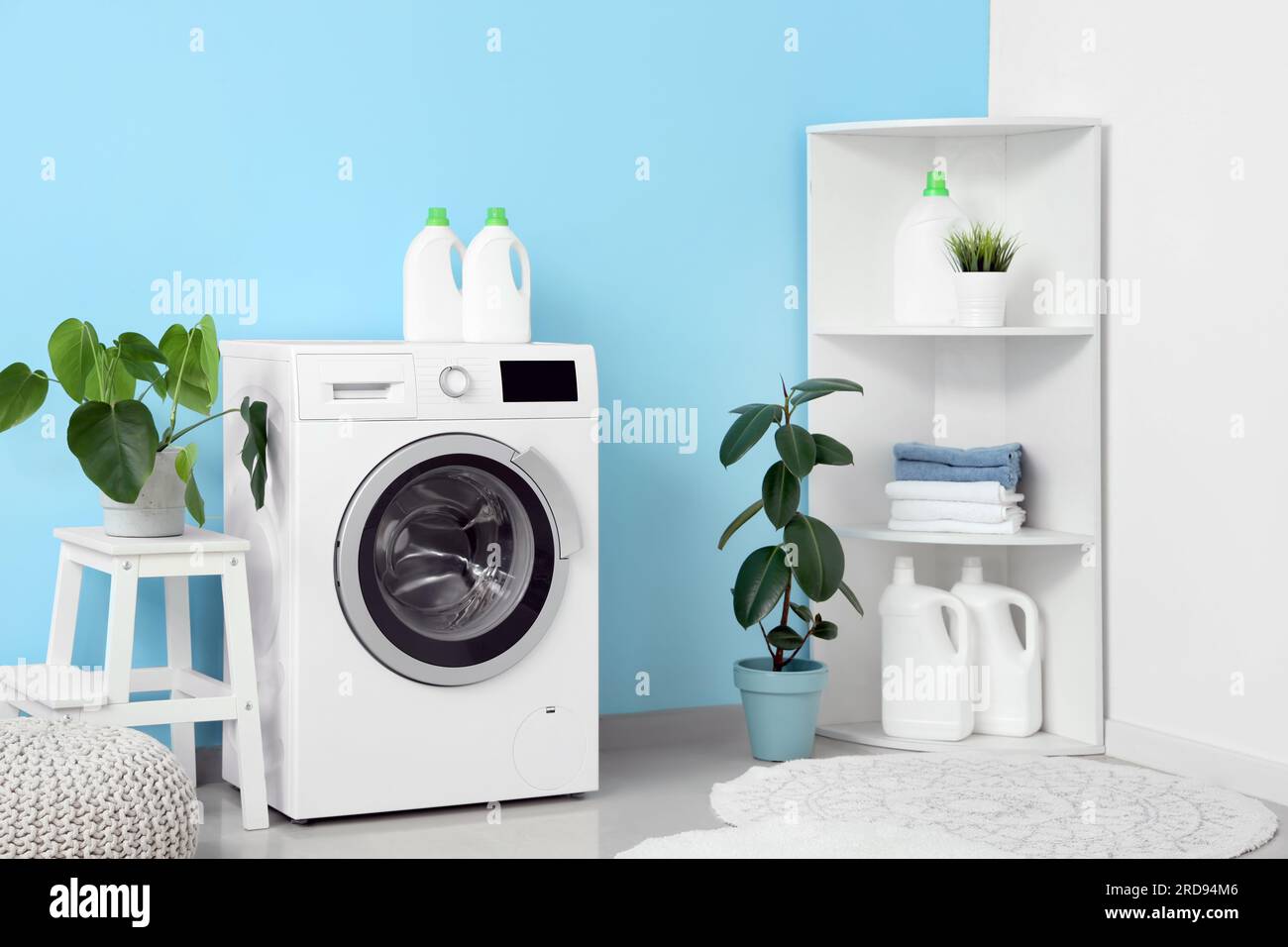 Washing machine, shelving unit, houseplants and pouf near blue wall