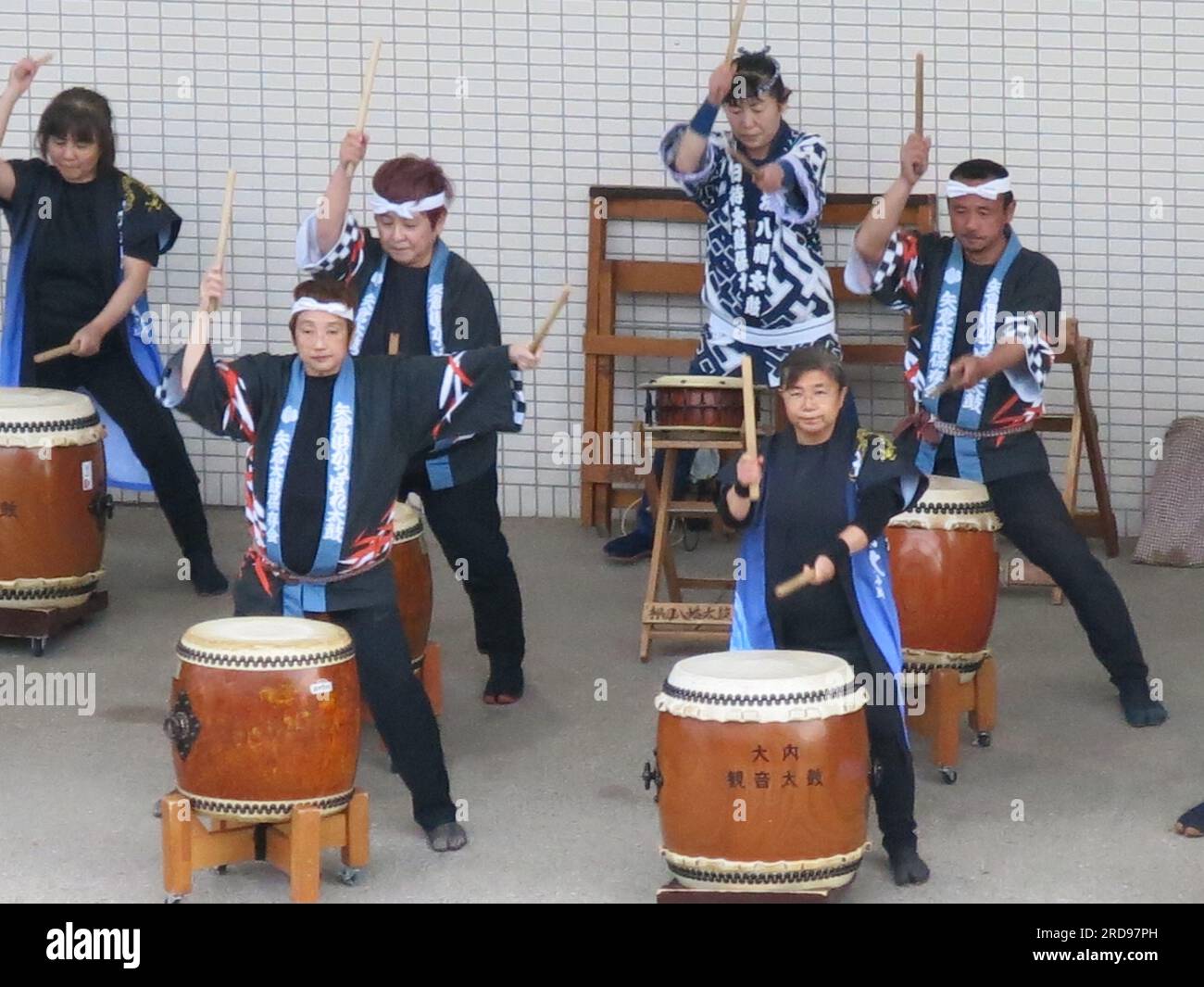 A group of Japanese drummers in traditional costume play their drums on
