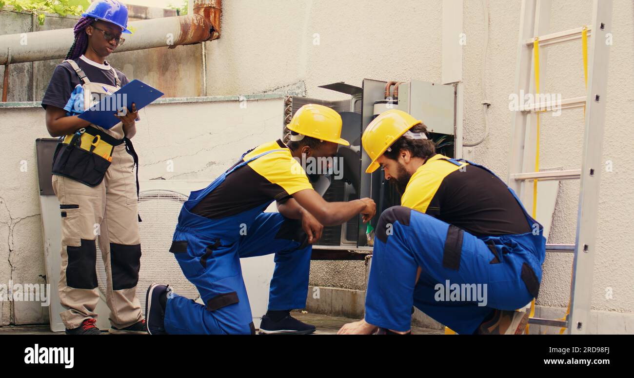 Expert african american technician cleaning layer of dirt and dust from condenser compressor coils while colleague uses manometers to check for refrigerant leaks and read pressure in hvac system Stock Photo