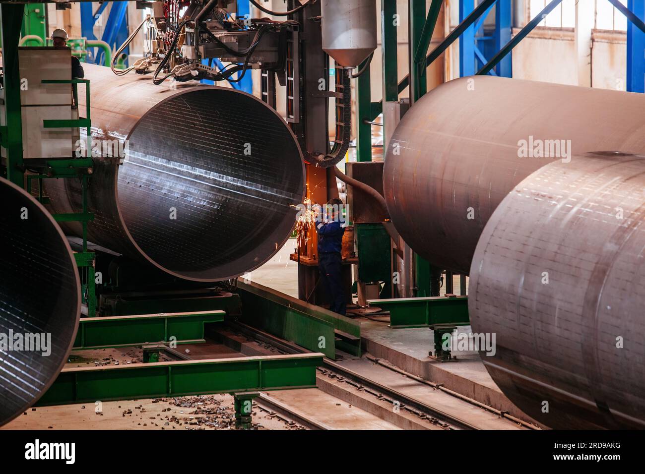 Worker cleans welded seam on steel pipe using grinding machine Stock