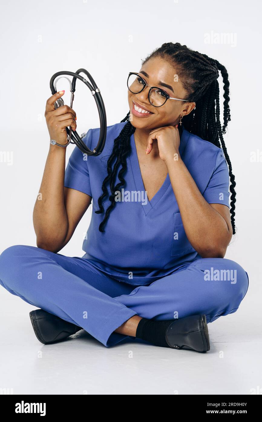 Portrait of a smiling female nurse or doctor in blue scrubs uniform sitting holding stethoscope Stock Photo