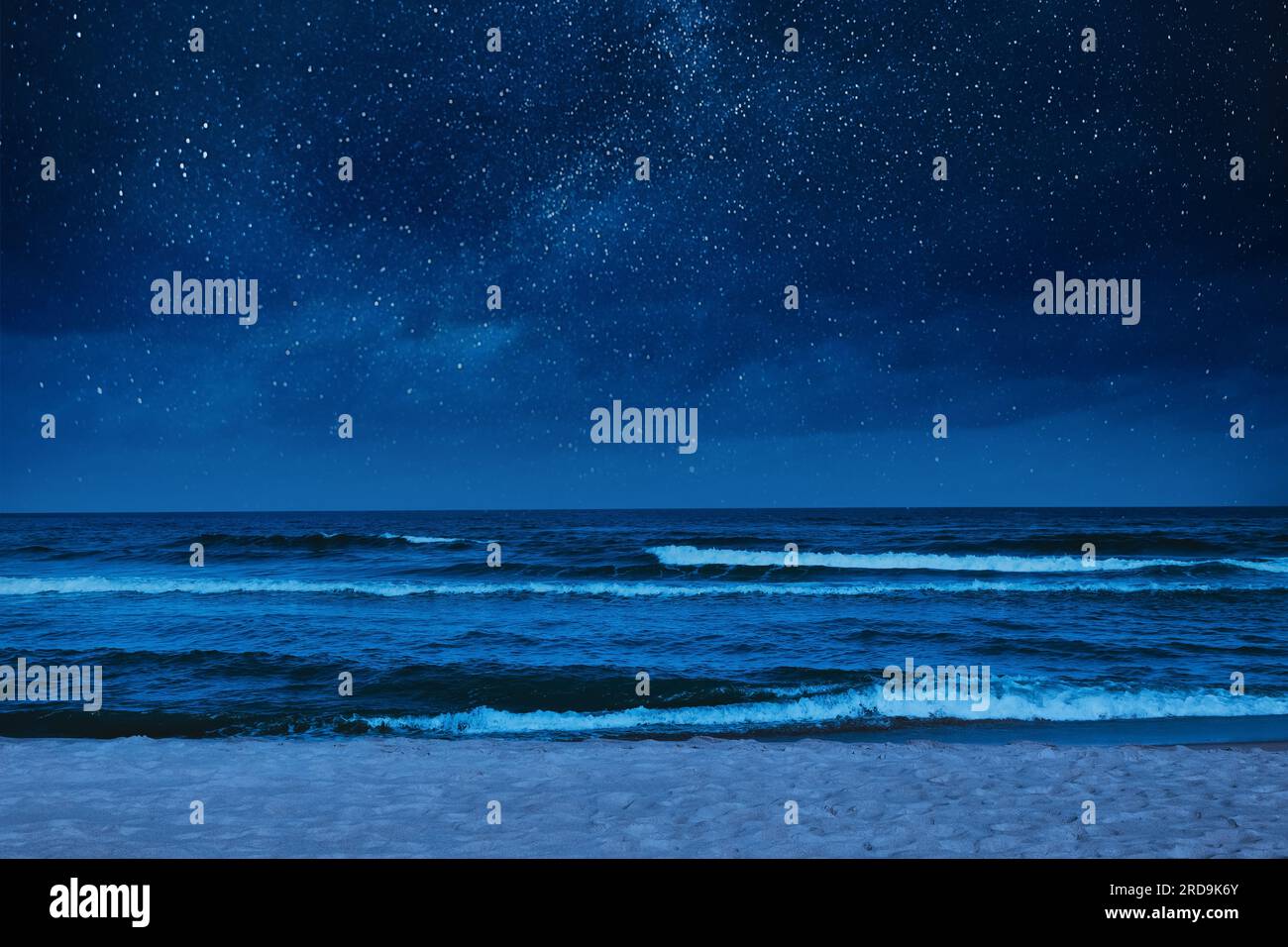 Sea waves rolling onto sandy beach under starry sky at night Stock Photo