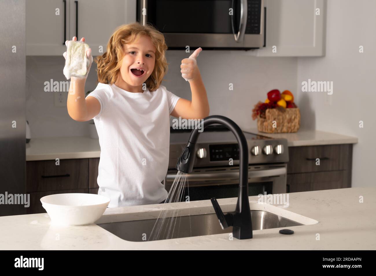Kid washing dishes in the kitchen interior. Child helping his parents
