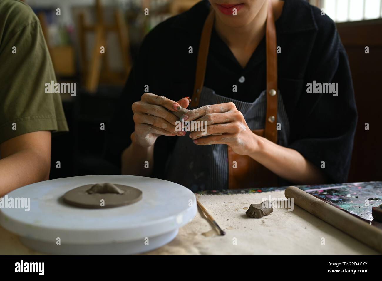 Craftspeople wearing aprons working with raw clay, shaping and decorating pottery in workshop Stock Photo