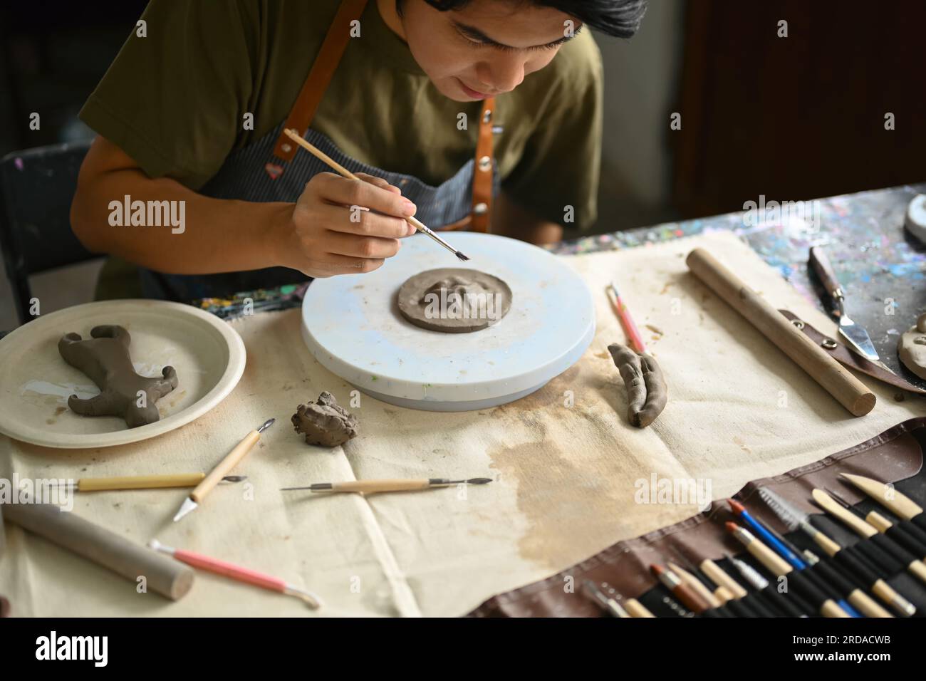 Man wearing apron sculpting clay plate on pottery wheel, creating handmade ceramics in art class